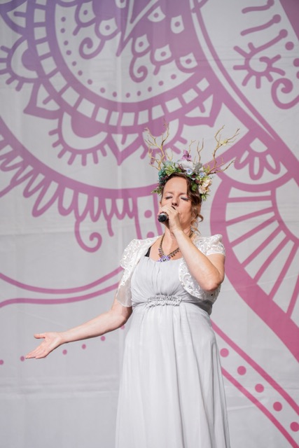 Lady in White dress singing on stage with mandala behind her